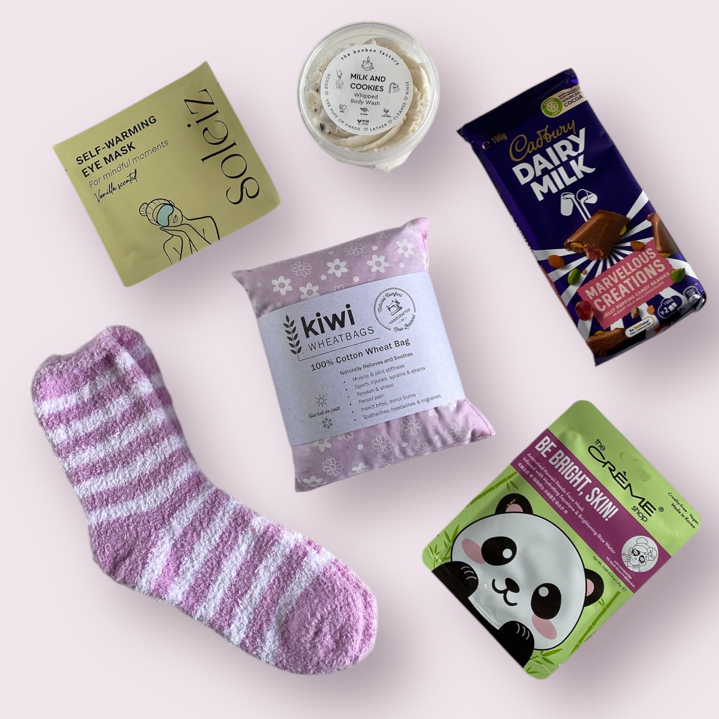 Contents of our self care gift box including, soleiz self warming eye mask, bon bon factory cookies and milk body wash, fluffy socks, kiwi wheat bag, cadbury dairy milk, the creme shop face mask.