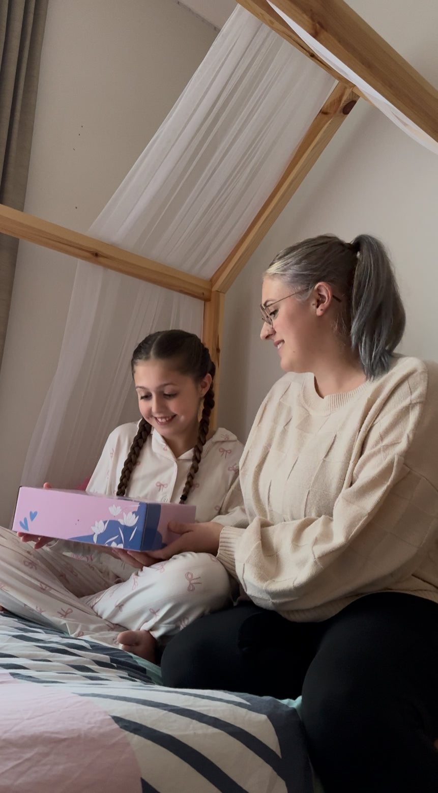 Mum and Daughter sitting on a bed with a giftbox.