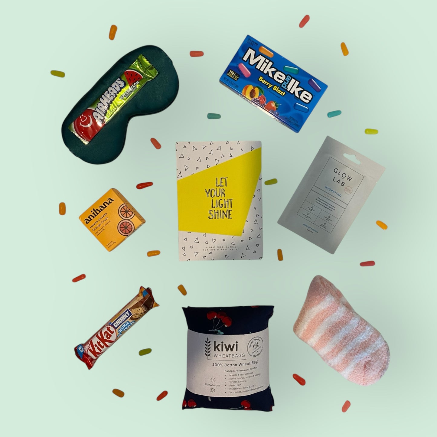 Contents of gift box displayed. Eye mask, airheads candy, Mike and Ike candy, anihana shower steamer, let your light shine gratitude journal, glow lab face mask, kit kat, kiwi wheat bag and fluffy socks.
