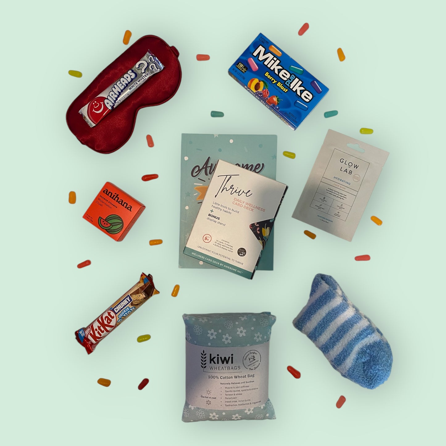 Contents of self care gift box, silk eye mask, american candy, anihana shower steamer, awesome ends in me gratitude journal, thrive daily wellness cards, glow lab face mask, kit kat chunky bar, kiwi wheatbag and fluffy socks.