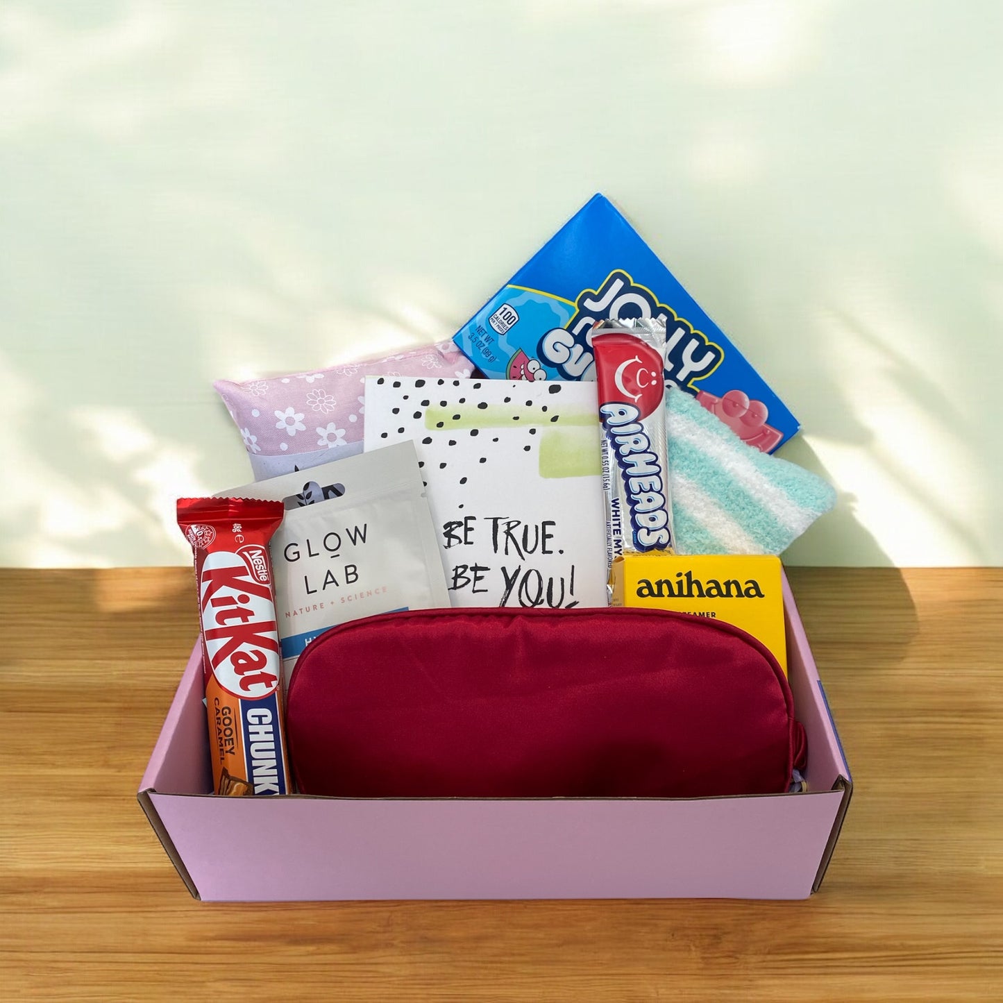 Beautiful gift box showing items. Kiw wheat bag, american candy, fluffy socks, gratitude journal, glow lab face mask, airheads candy, kit kat, eye mask and anihana shower steamer.