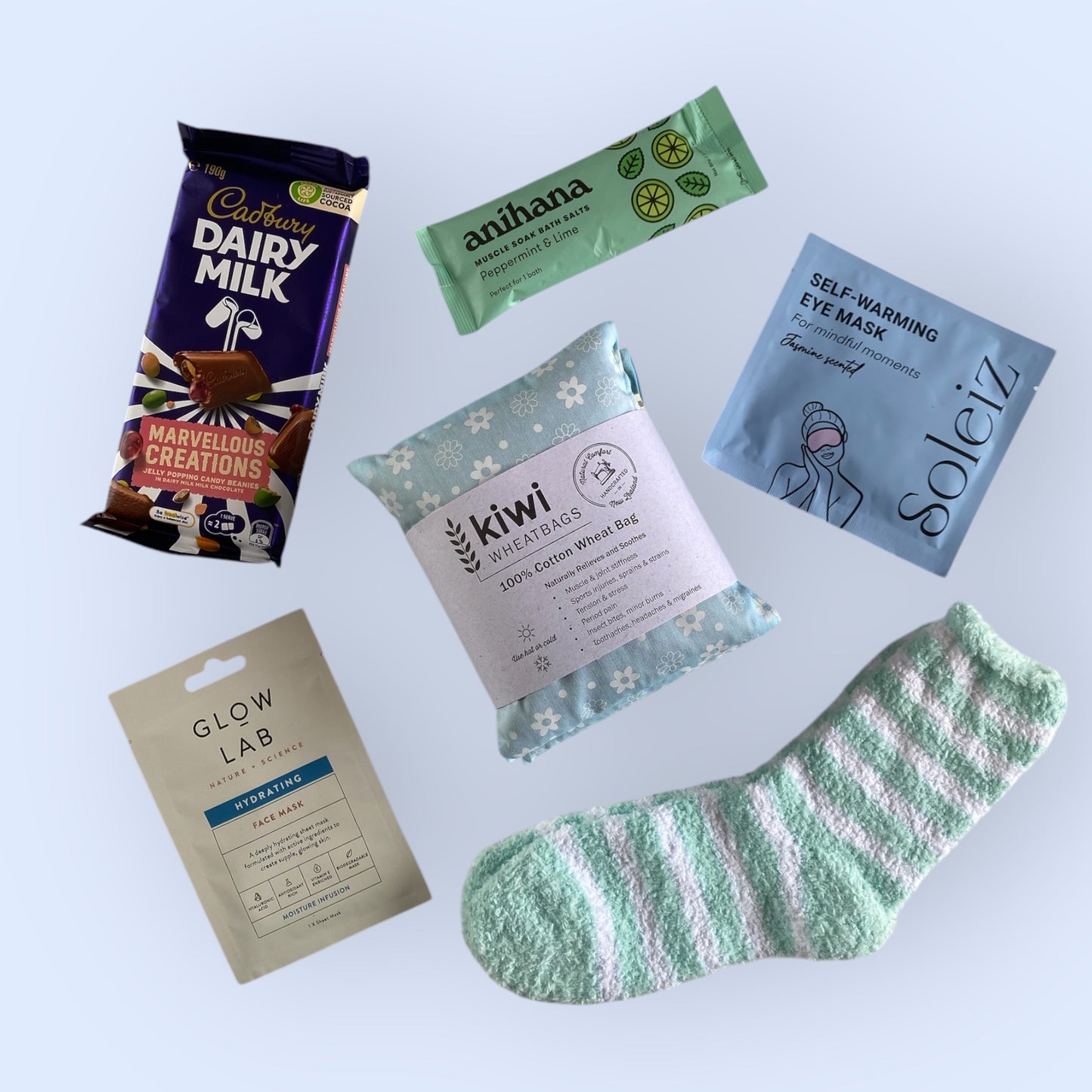 Contents of our self care gift box including, cadbury dairy milk, anihana bath salts, soleiz self warming eye mask, kiwi wheat bag, glow lab face mask and fluffy socks.
