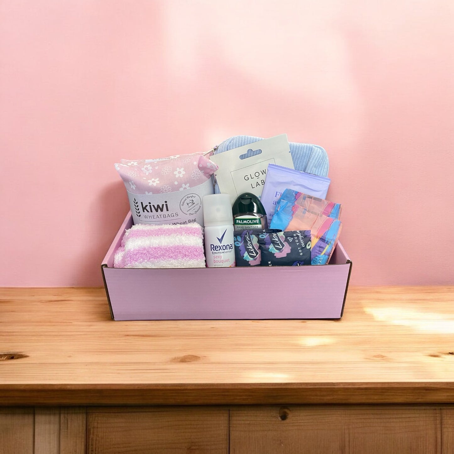 Period products in a gift box, wheatbag, fluffy socks, face mask, purse for pads, pads, mini spray, hand sanitiser and flushable wipes.