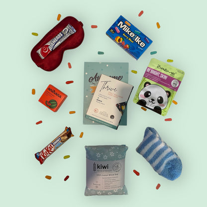 Contents of self care gift box, silk eye mask, american candy, anihana shower steamer, awesome ends in me gratitude journal, thrive daily wellness cards, glow lab face mask, kit kat chunky bar, kiwi wheatbag and fluffy socks.