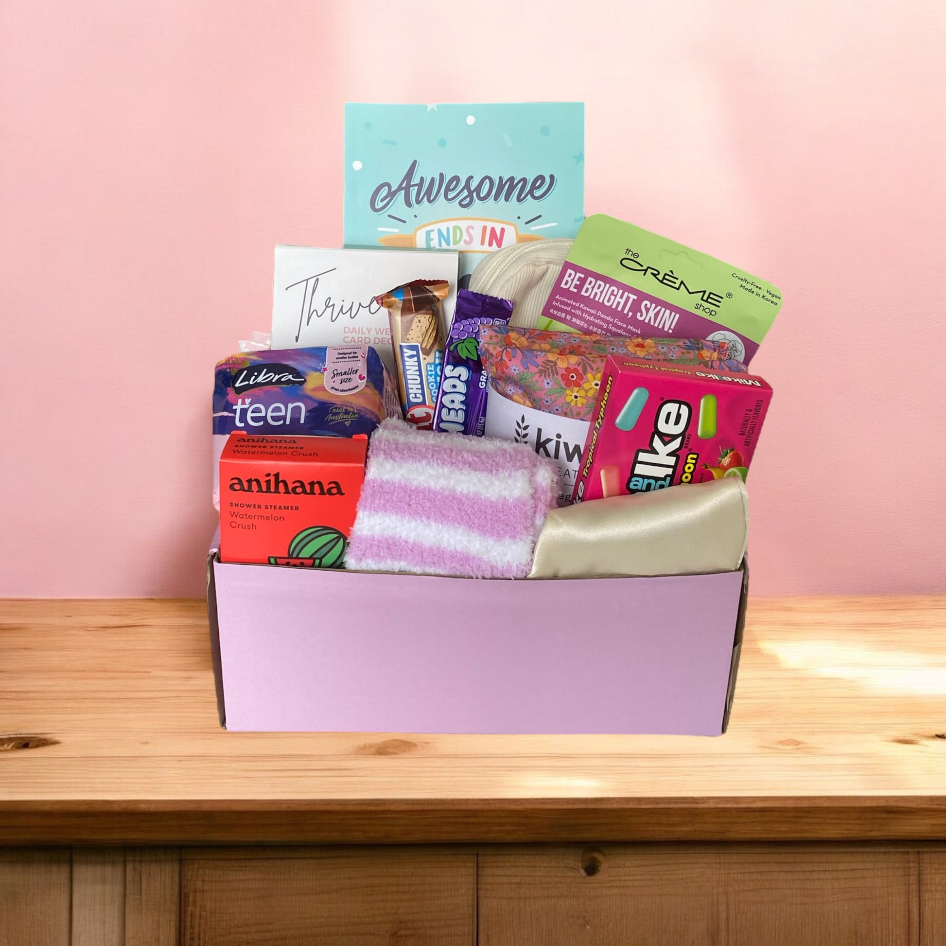 Items of gift box on disply in gift box. Awesome ends in me journal, american candy, thrive wellness cards, kiwi wheatbags, glow lab face mask, kit kat, airheads, eye mask, libra teen pads, fluffy socks and anihana shower steamer.
