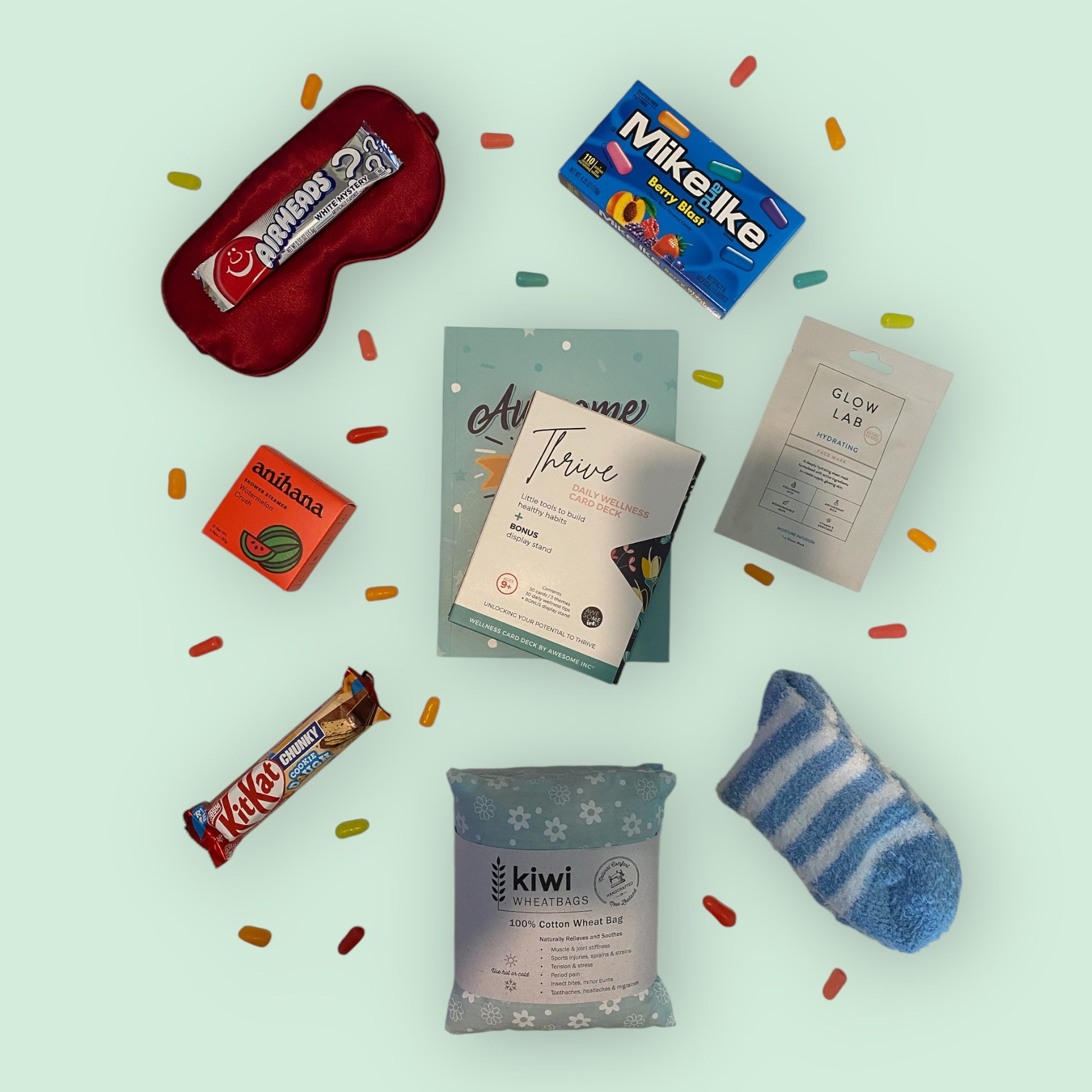 Contents of self care gift box, silk eye mask, american candy, anihana shower steamer, awesome ends in me gratitude journal, thrive daily wellness cards, glow lab face mask, kit kat chunky bar, kiwi wheatbag and fluffy socks.