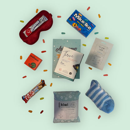 Contents of self care gift box, silk eye mask, american candy, anihana shower steamer, awesome ends in me gratitude journal, thrive daily wellness cards, glow lab face mask, kit kat chunky bar, kiwi wheatbag and fluffy socks.