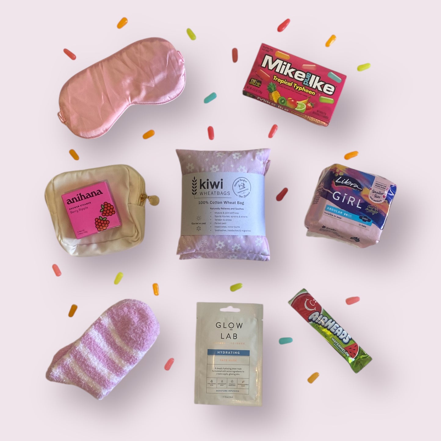 Items of gift box on display. Eye mask, Mike and Ike american candy, little purse, anihana shower steamer, kiwi wheatbag, libra teen pads, fluffy socks, glow lab face mask and airheads candy bar.