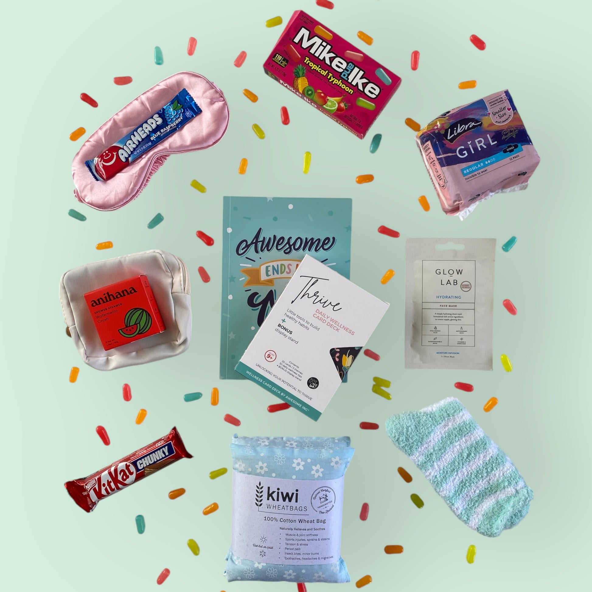 Contents of tween gift box on display. Eye mask, airheads candy, Mike and Ike candy, libra teen pads, anihana shower steamer, little purse, awesome ends in me journal, thrive wellness cards, glow lab face mask, kit kat, kiwi wheatbag and fluffy socks.