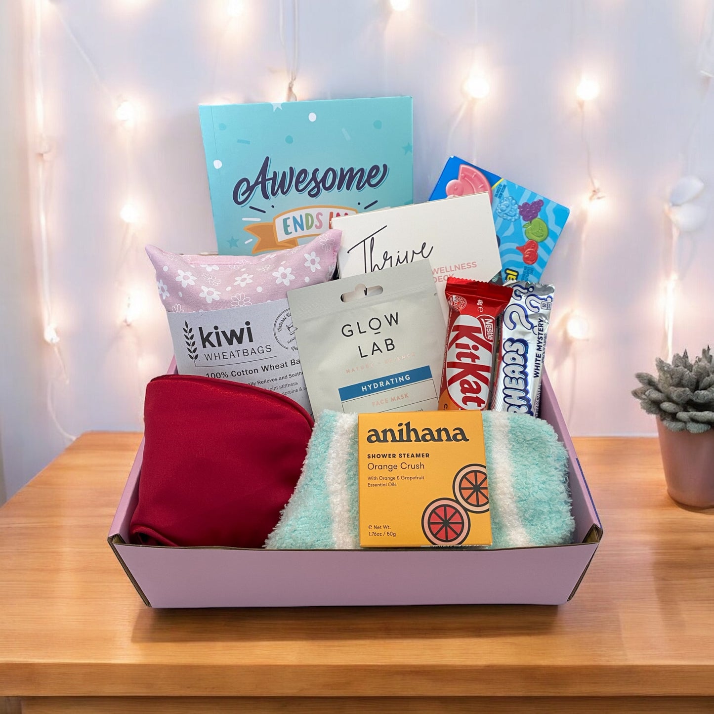 Gift Box shocasing items. Awesome ends in me gratitude journal, Thrive wellness cards, Jolly rancher candy,kiwi wheat bag, glow lab face mask, kit kat , air heads candy, eye mask, fluffy socks and anihana shower steamer.