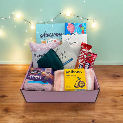 Items of gift box on disply in gift box. Awesome ends in me journal, american candy, thrive wellness cards, kiwi wheatbags, glow lab face mask, kit kat, airheads, eye mask, libra teen pads, fluffy socks and anihana shower steamer.