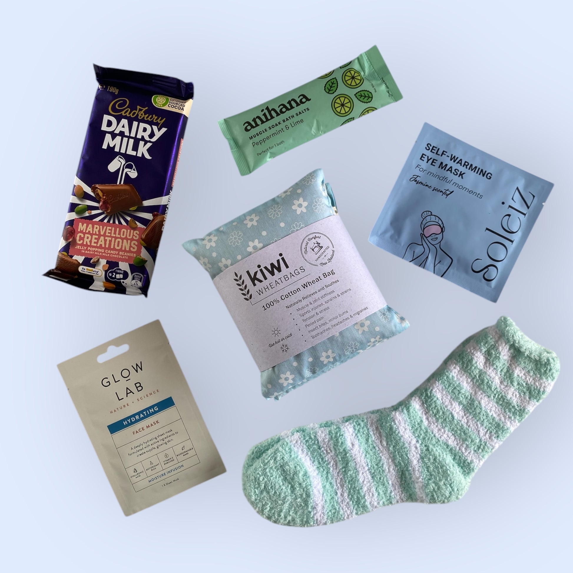 Contents of our self care gift box including, cadbury dairy milk, anihana bath salts, soleiz self warming eye mask, kiwi wheat bag, glow lab face mask and fluffy socks.